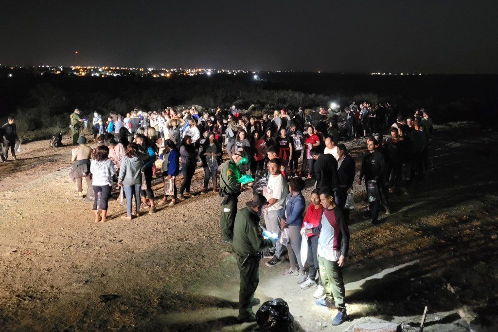 Border Patrol stands near a large group of migrants.