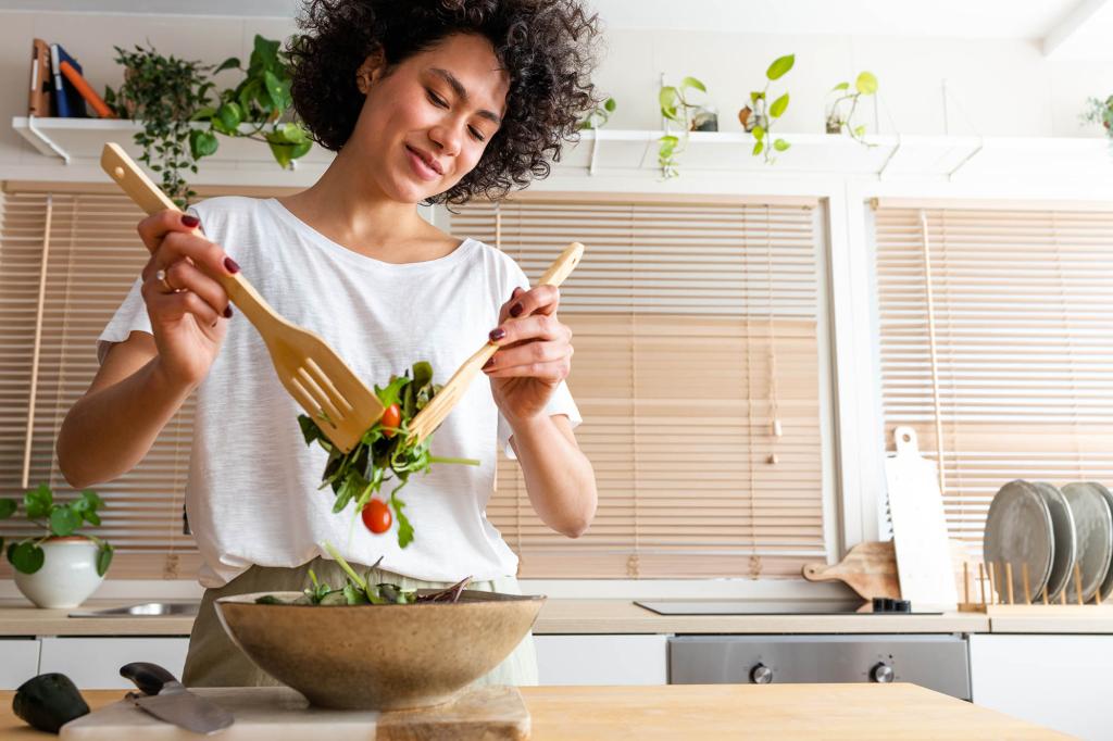 Happy young multiracial woman mixing bowl of fresh salad. Copy space.Healthy lifestyle concept.