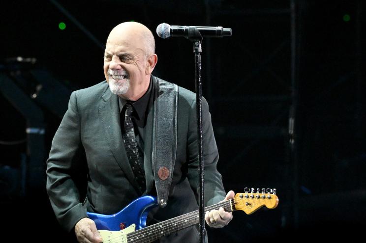 Singer Billy Joel rocks out onstage with a guitar.