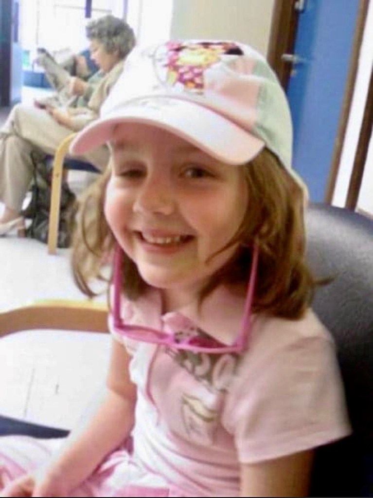 Young girl in pink shirt and cap smiling at camera.