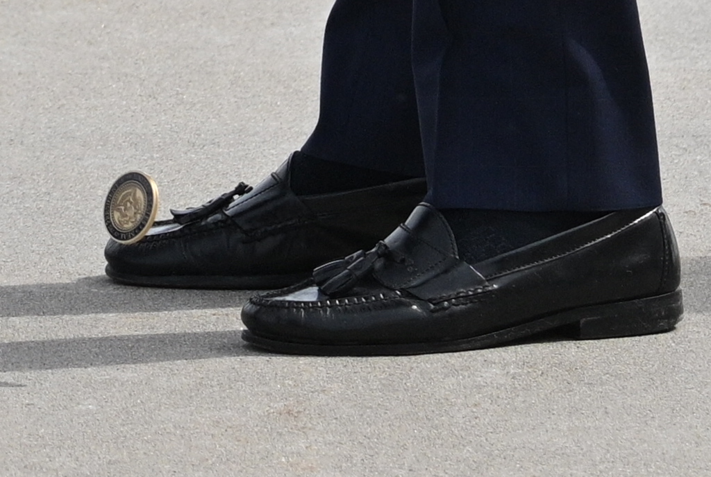 A challenge coin drops to the ground at President Biden's feet Monday, April 3, 2023. 