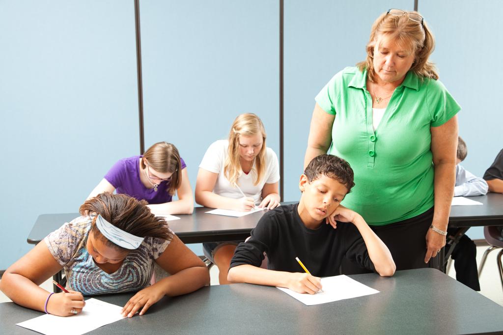 Teacher looks over the shoulder of a boy taking a test