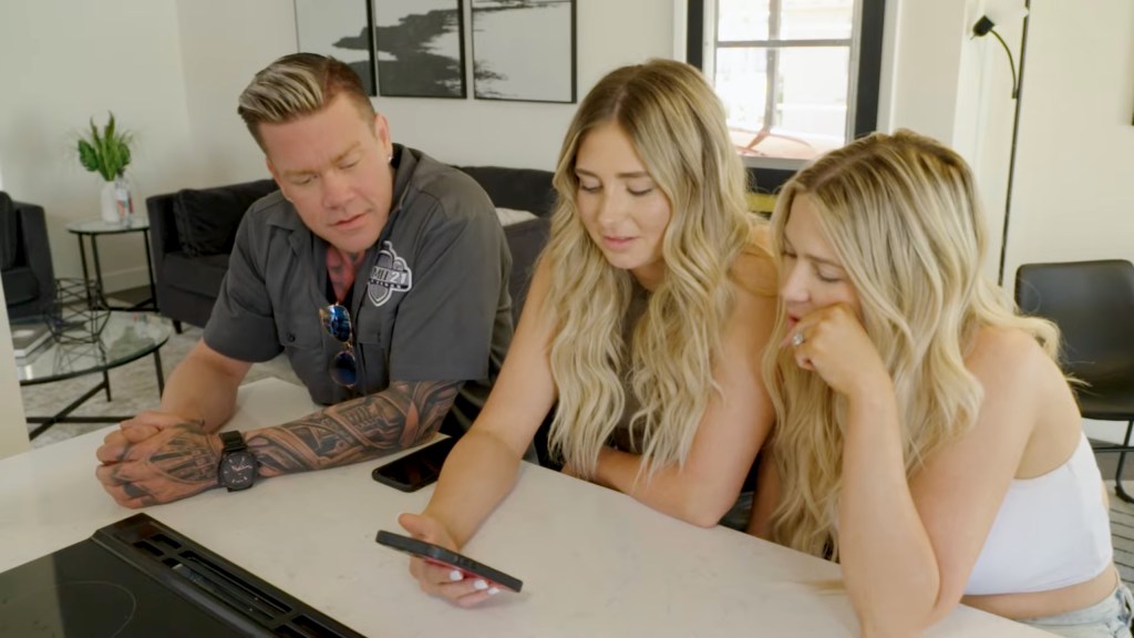 Man and two blonde women sitting at kitchen bench.