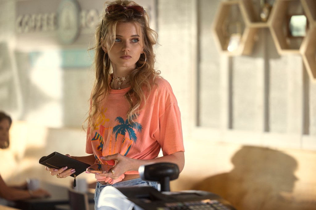 Abbey Lee standing in a room holding a phone looking serious. 