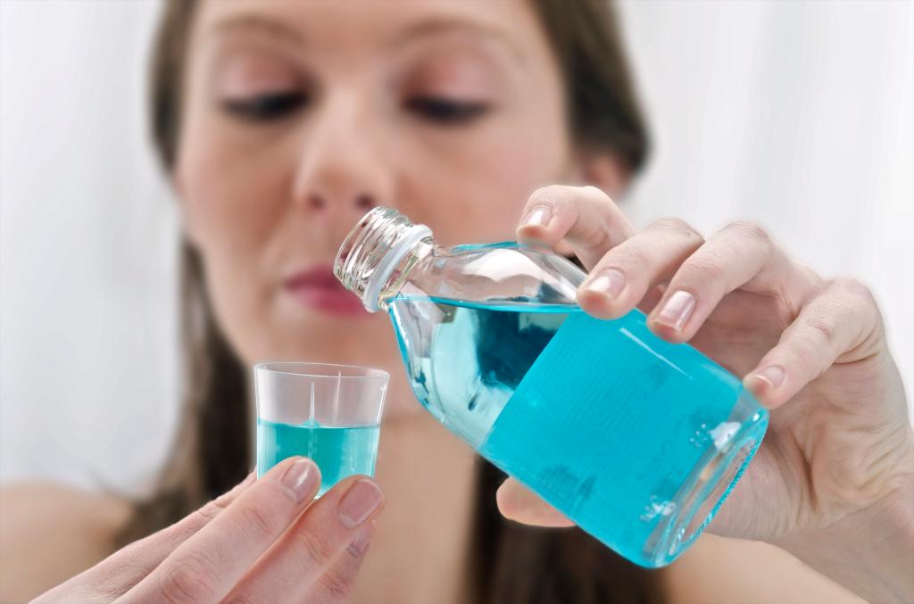 Woman pouring mouthwash into little cup