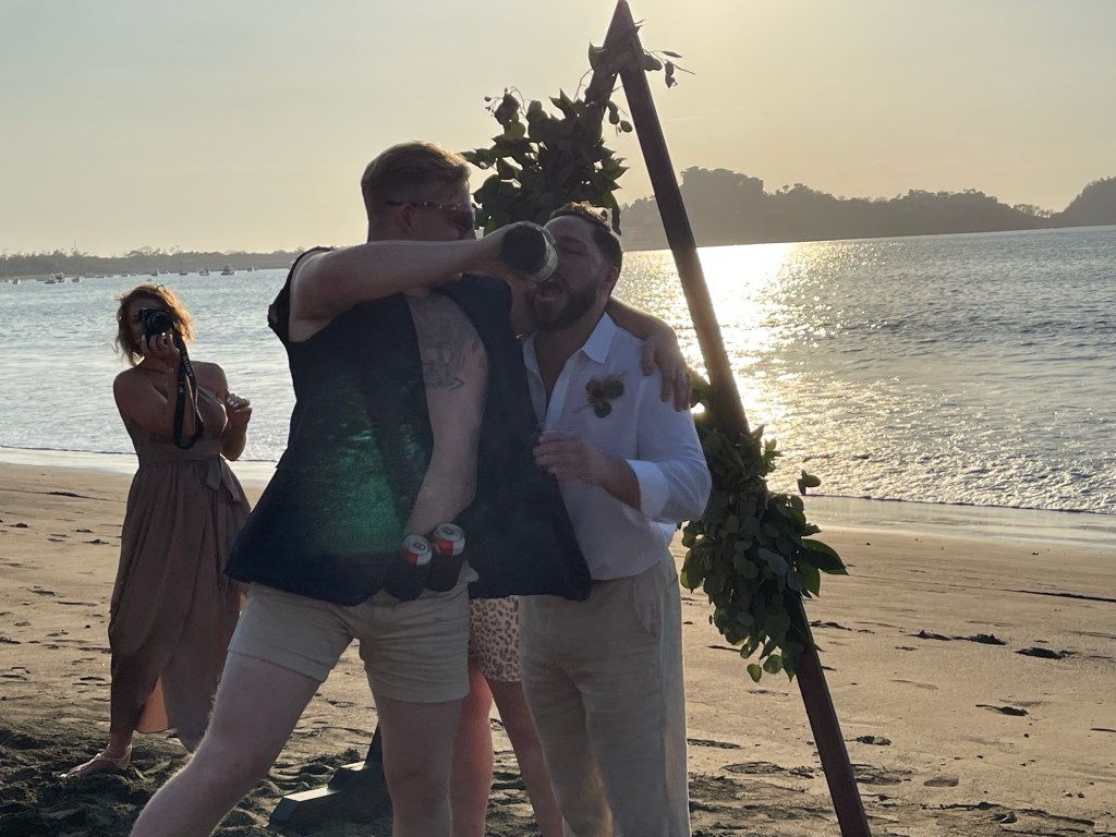 Austin Hoyt (left) pouring a shot into Austin Tompkins' mouth during Tompkins' March 3, 2023 destination wedding in Costa Rica. 