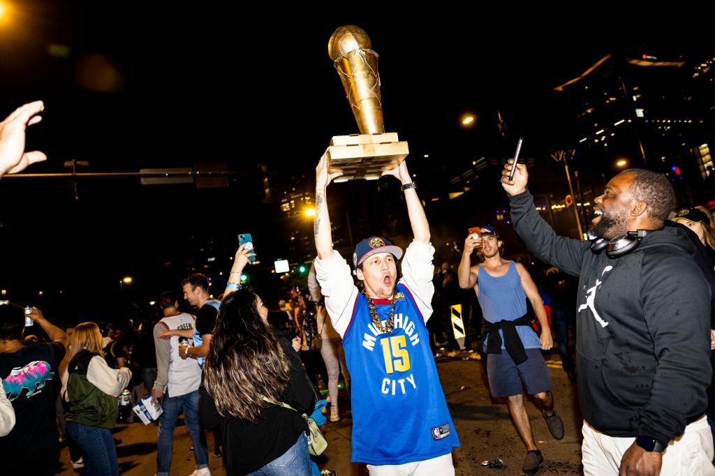 A Denver Nuggets fan lifts a trophy in the air in the streets of downtown Denver, Colo., following the franchise first NBA Championship win.