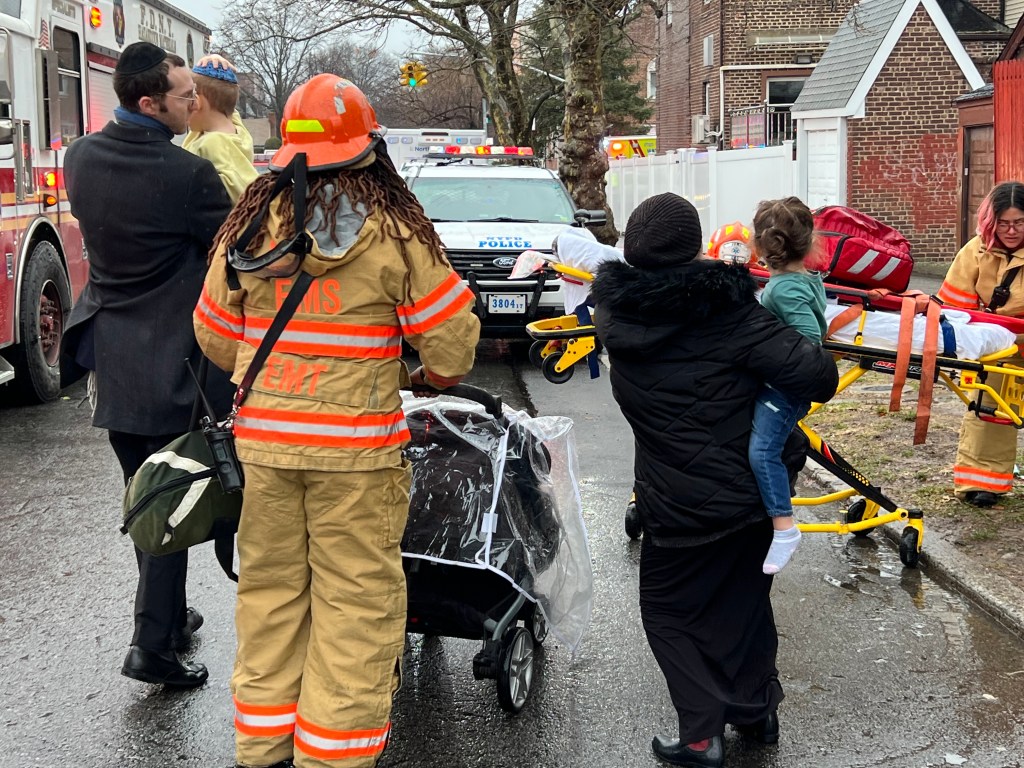 EMTs respond to a scene where people are holding children and a stretcher is being wheeled out.