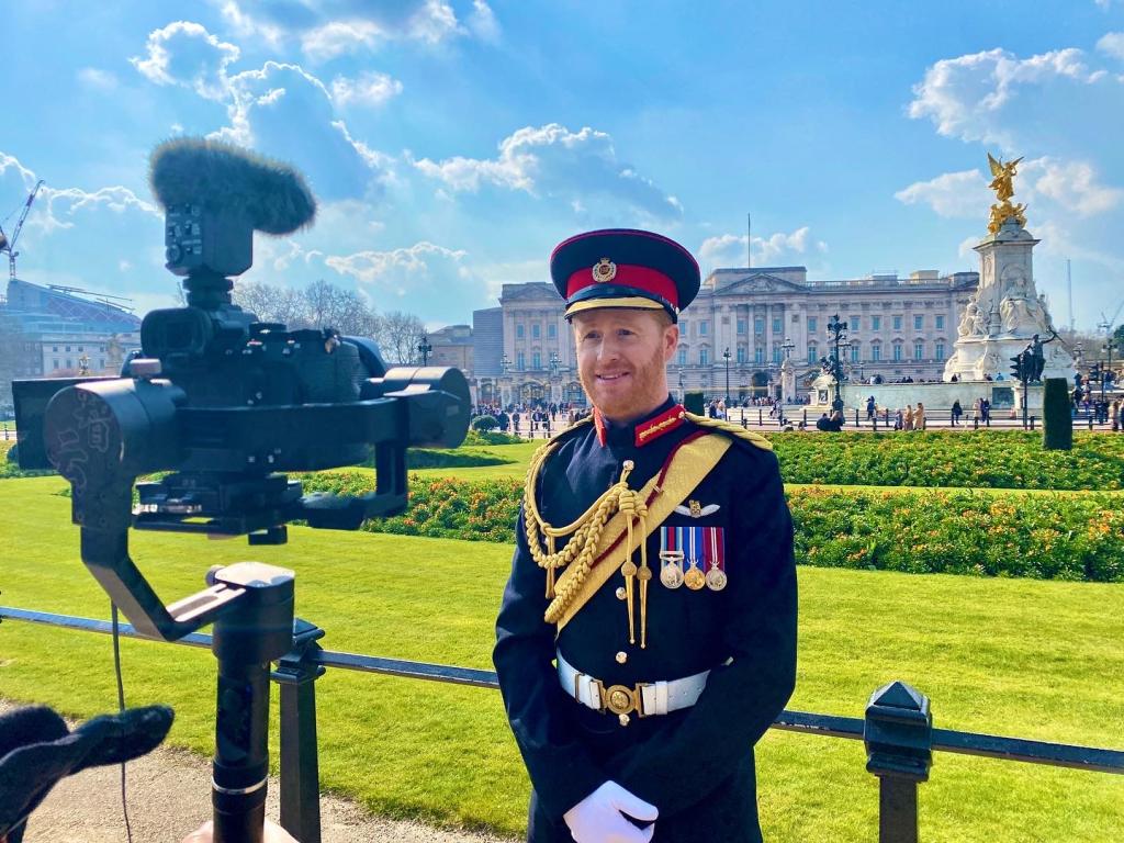 Man dressed up as Prince Harry in front of palace.