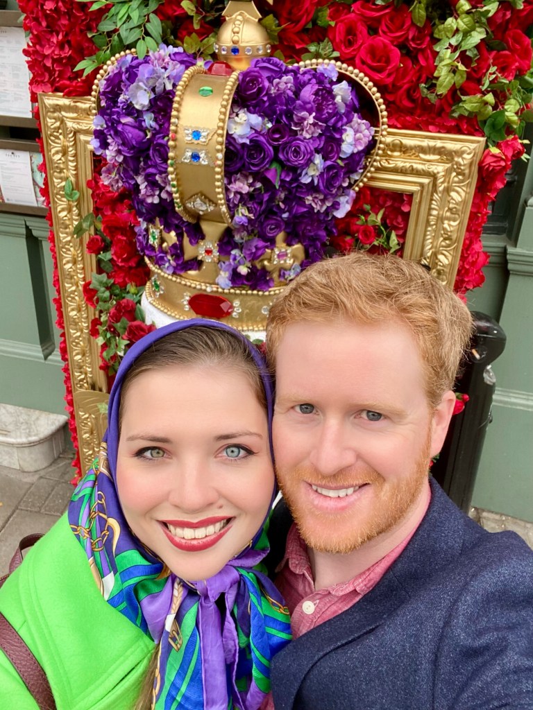 Young woman dressed in bright colors selfie with red haired man in navy glazer. 