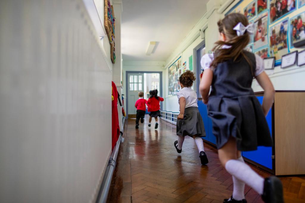 Elemary school students running down a hallway while at school.