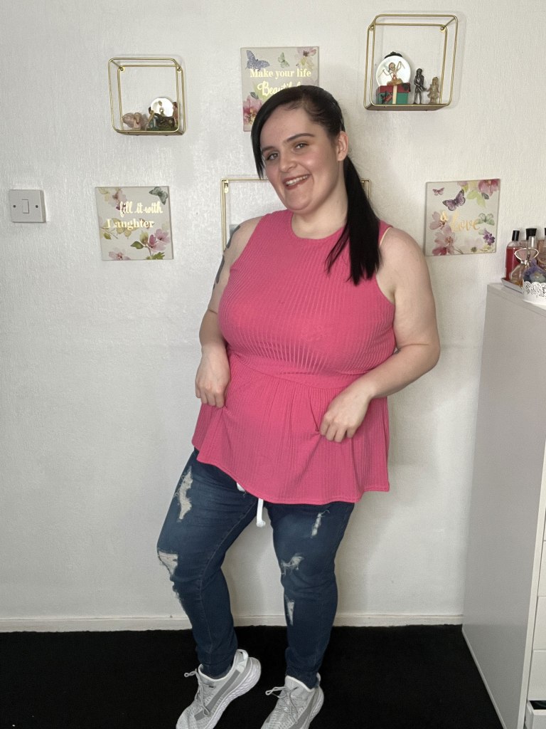 Photo of a woman wearing jeans and a pink tank top. 