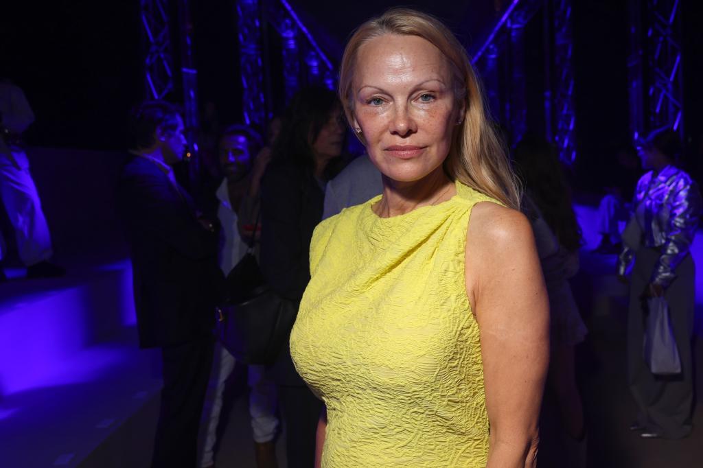 Photo of Pamela Anderson looking at the camera and posing in a yellow dress. 