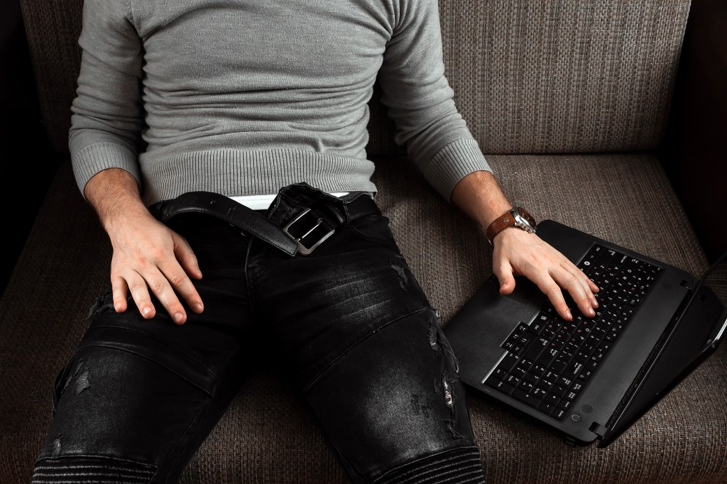 A man watches an adult video on a laptop while sitting on the couch. The concept of porn, men's needs, pervert, lust, desire, loneliness.