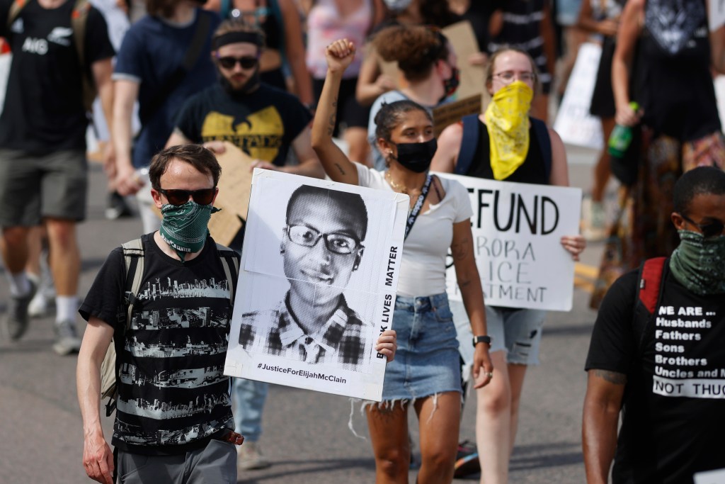 In this June 27, 2020 file photo, demonstrators carry placards as they walk down Sable Boulevard during a rally and march over the death of Elijah McClain in Aurora, Colo. 