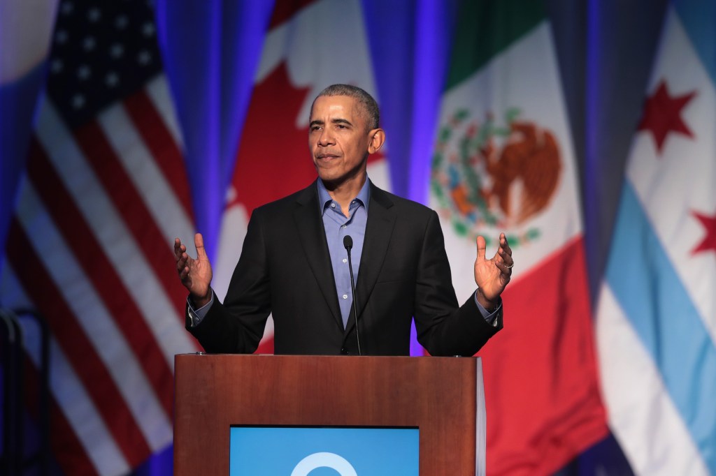 Barack Obama stands at a podium with flags of different countries behind him. 