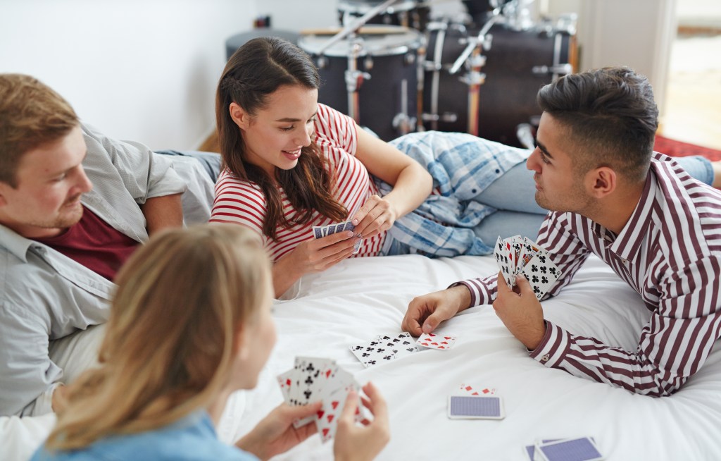 Young friends playing cards while relaxing on bed at leisure