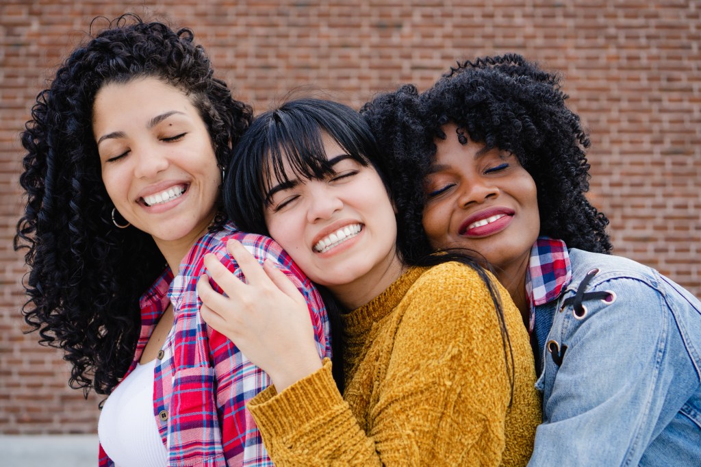 Three young, interracial, Latina and Hispanic interracial friends hugging with eyes closed.