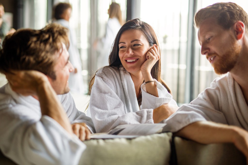 Group of happy multiethnic people enjoying wellness relax weekend. Woman with two handsome men in bedroom. Polyamory concept