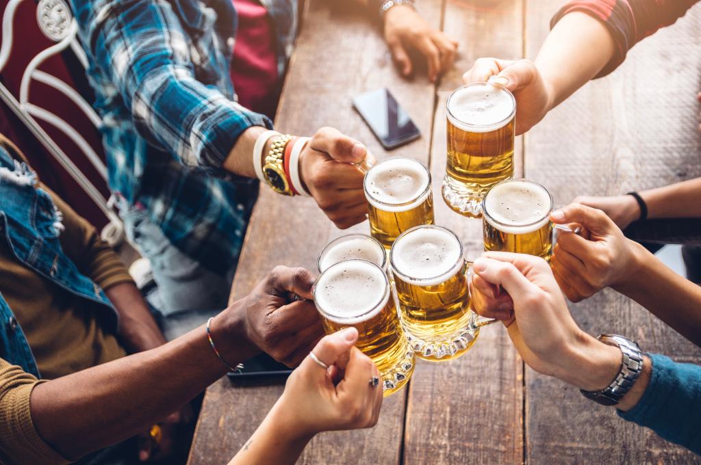 Group of people enjoying and toasting a beer in brewery pub - Friendship concept with young people having fun together.