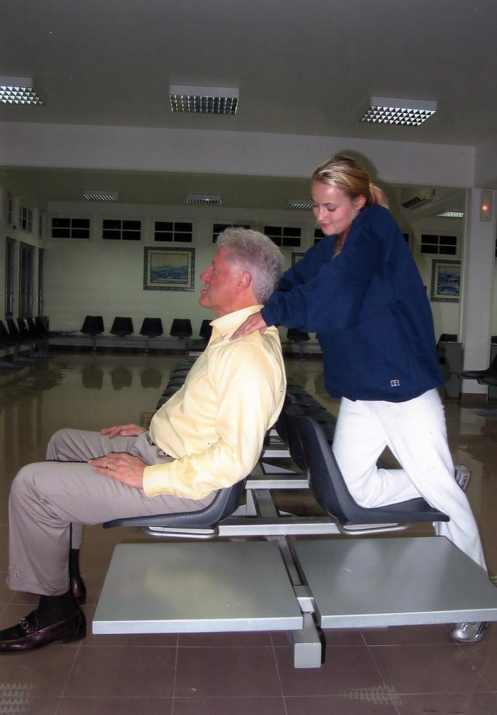 Chauntae Davies stands behind a seated Bill Clinton and massages his neck 