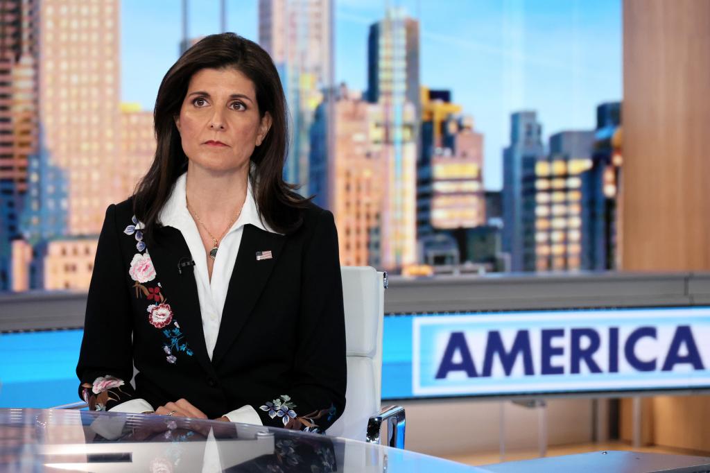 Nikki Haley sitting in a chair in a TV studio with the word "America" behind her 