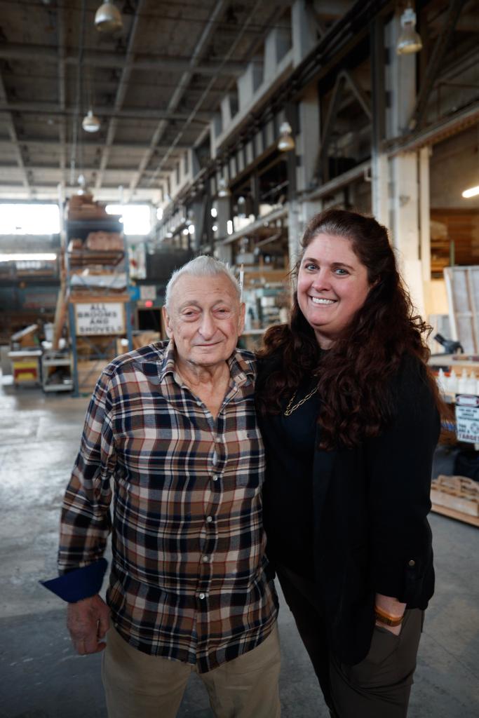 Stephen DeMaria and Nicole Stiegelbauer smile together in a construction shop. 