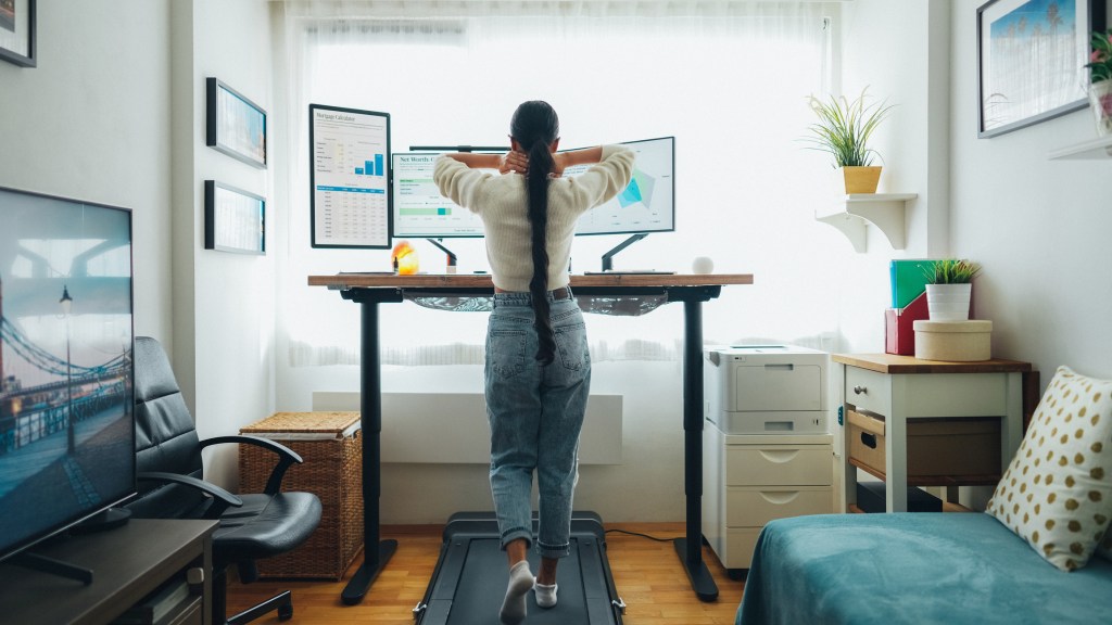 Woman walking on under desk treadmill in front of computers