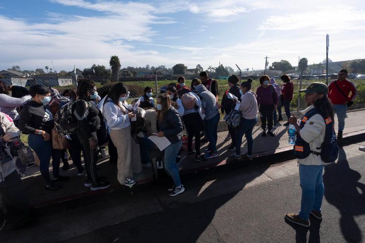 Migrants standing on sidewalk, following release from a processing facility due to lack of funding.