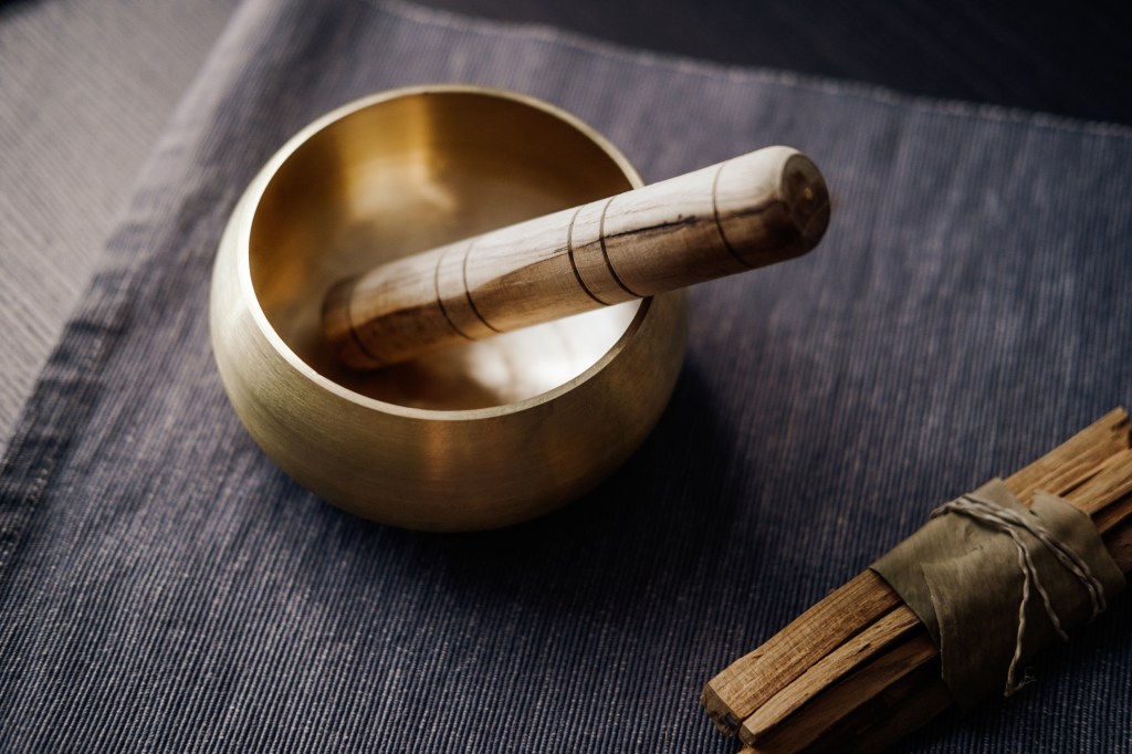 Bronze Tibetan singing bowl with wooden stick and palo santo wood on cloth - used for sound healing and therapy - stress reduction tool.