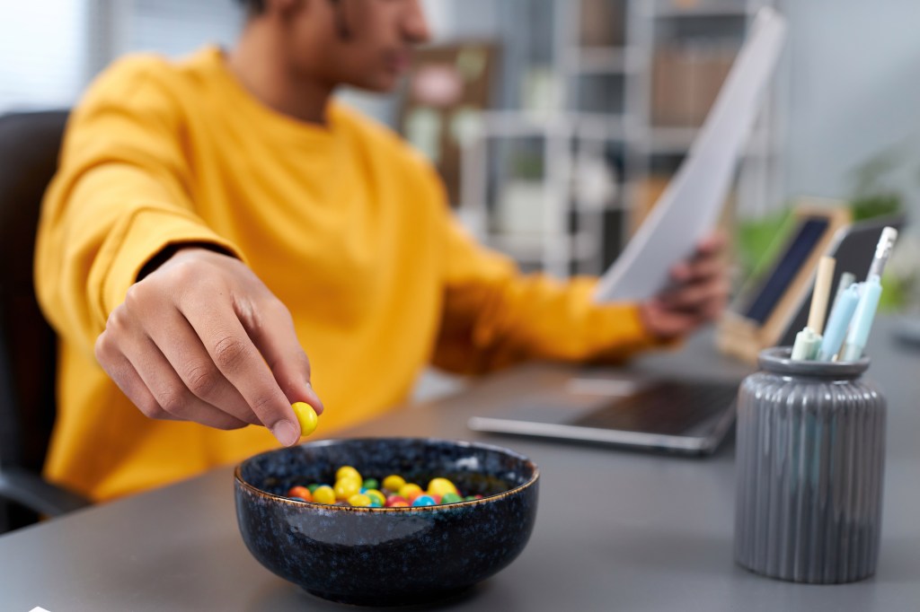 Young man holding colorful candy in hand while working or studying at home.