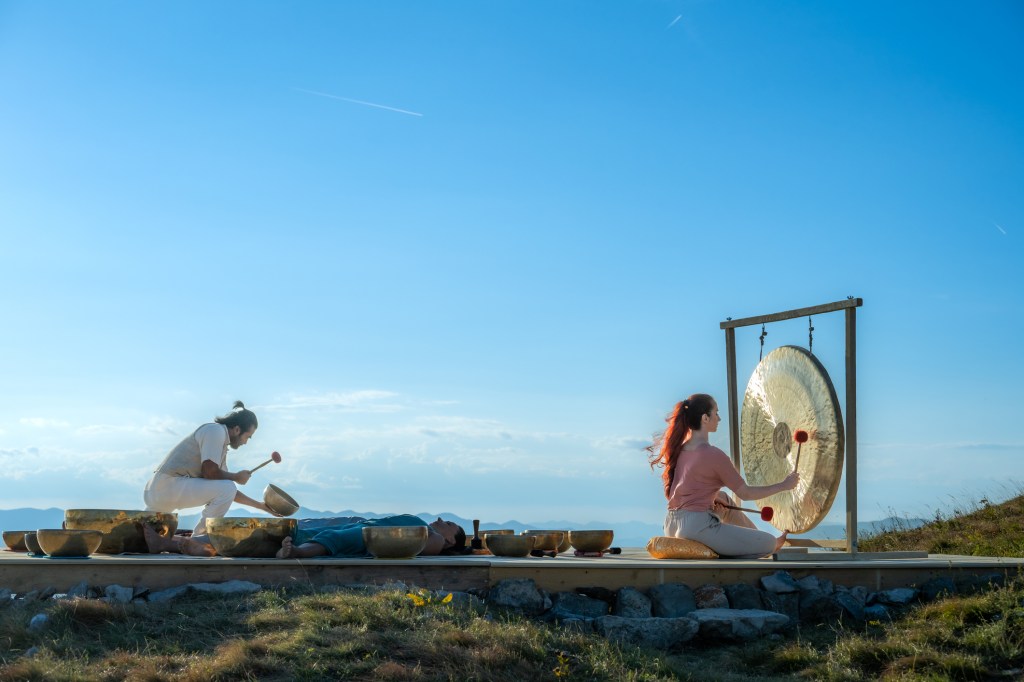 Man and woman playing bronze gong under blue sky, music therapy session. Singing bowls meditation and relaxation concept.