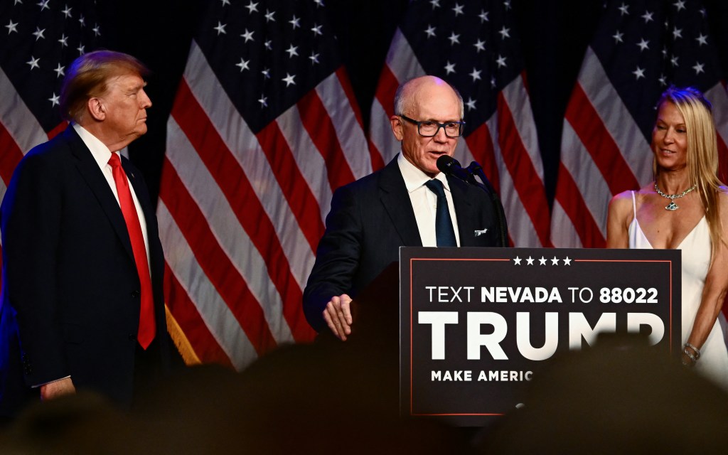 Woody Johnson speaking at a podium, next to Donald Trump and Suzanne Johnson. American flags hang in the background