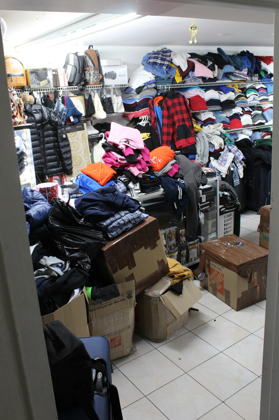 A room with apparent stolen goods. Clothes are piled up and there are boxes in the foreground