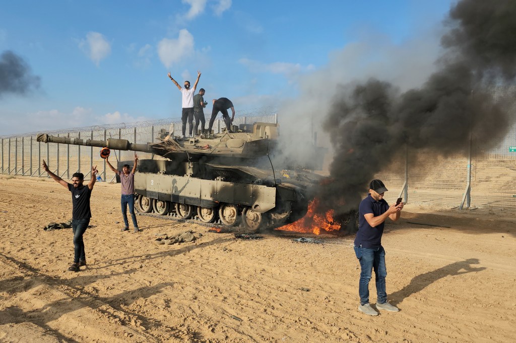 Hamas supporters stand on a burning tank at the Gaza Strip fence east of Khan Younis Saturday, Oct. 7, 2023.