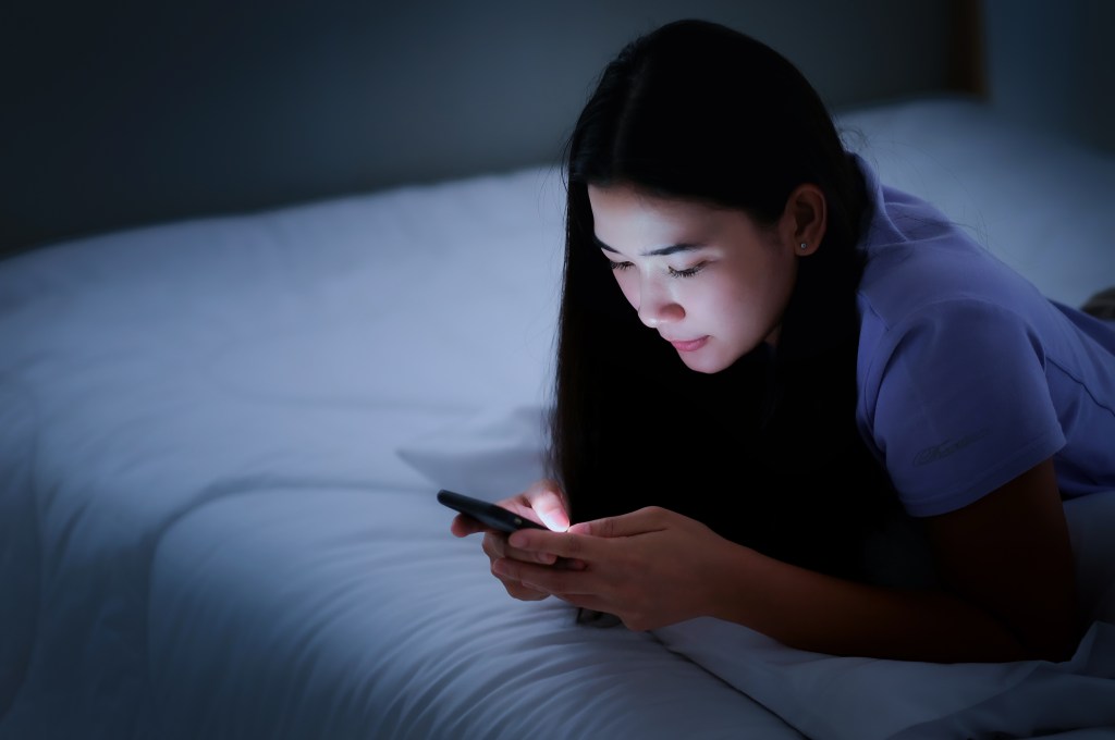 Woman looks at her phone in bed.
