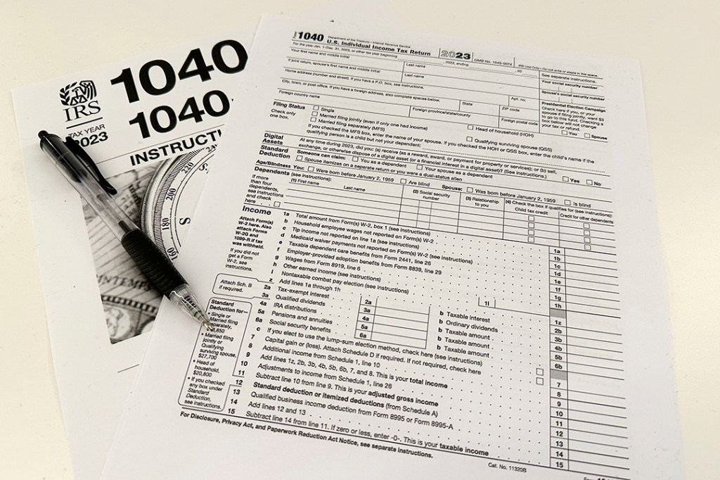 Internal Revenue Service 2023 1040 tax form, instructions, pen, and money on a table, symbolizing the 2026 tax season and new audit risks for certain businesses and millionaires.