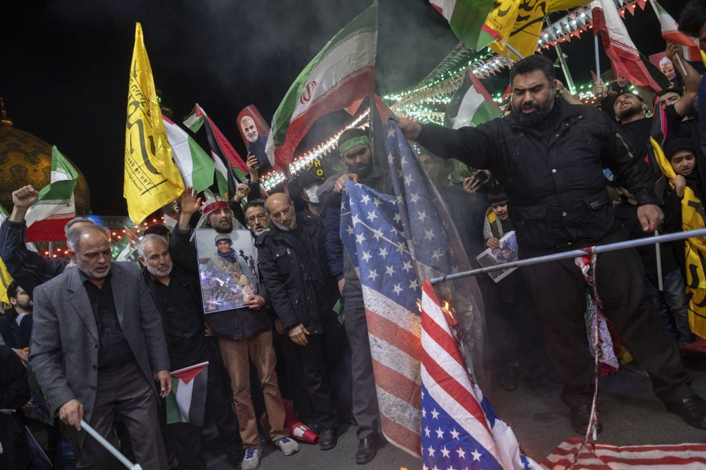 Iranian protesters are preparing to set U.S. flags on fire while one of them holds up a portrait of the former commander of the Islamic Revolutionary Guard Corps' (IRGC) Quds Force, General Qassem Soleimani.