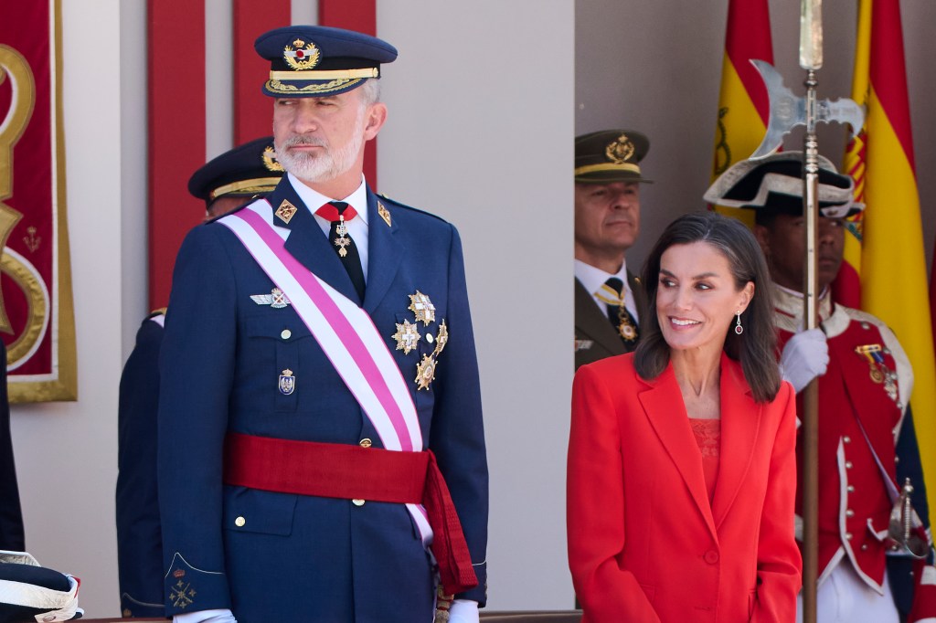 King Felipe of Spain wears full regalia as he stands next to Queen Letizia, in a red suit.