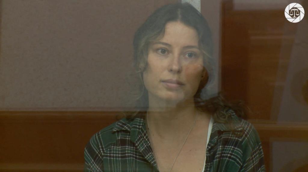 The court in the Urals city of Yekaterinburg published a short video of Ksenia Karelina sitting in a glass cage, wearing jeans and a green plaid shirt.