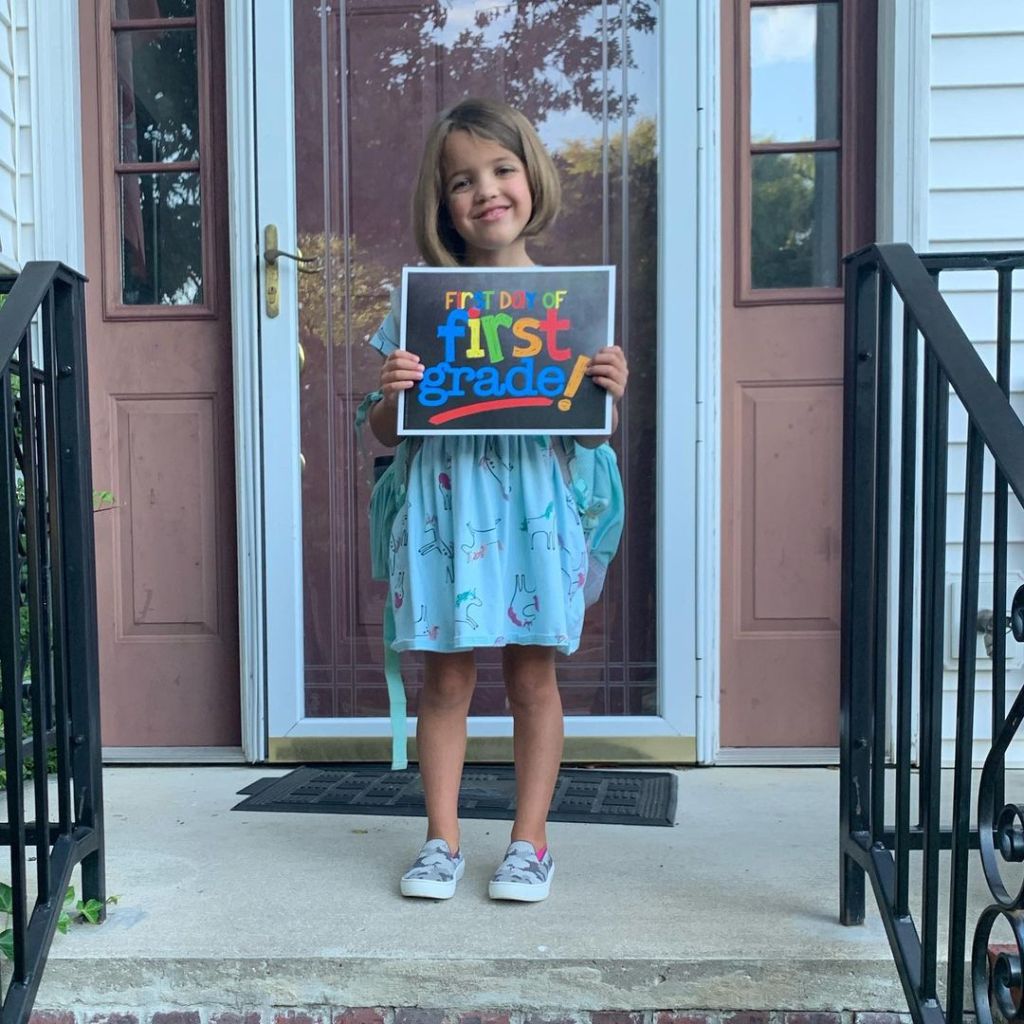 A little girl standing on her front stoop holding a sign that says "the first day of first grade"