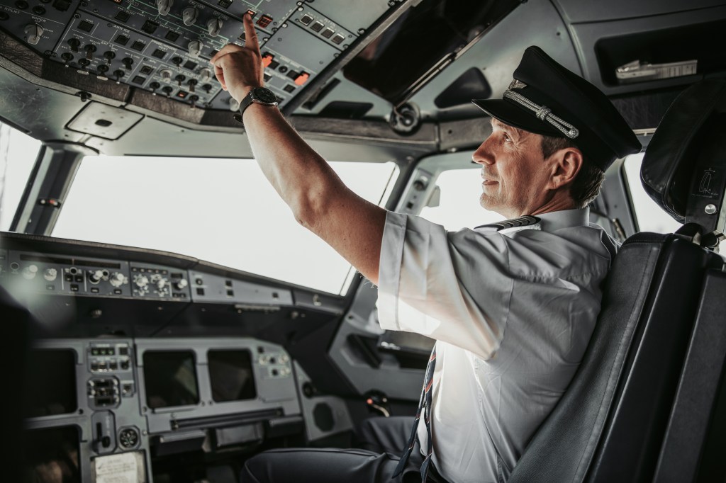 Pilot in uniform concentrating and pushing buttons on control panel in aircraft cabin