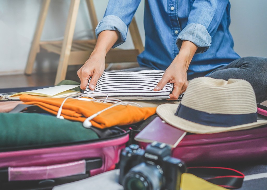 A person smartly packing clothes into a suitcase for a budget-friendly trip