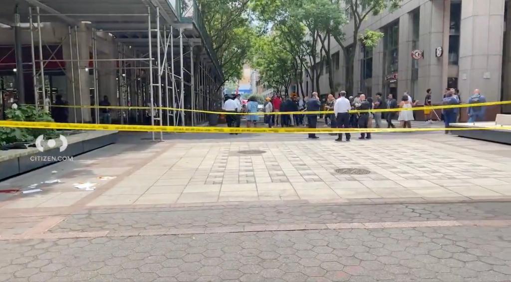 A large crowd in the background in the same courtyard with crime scene tape in the foreground.