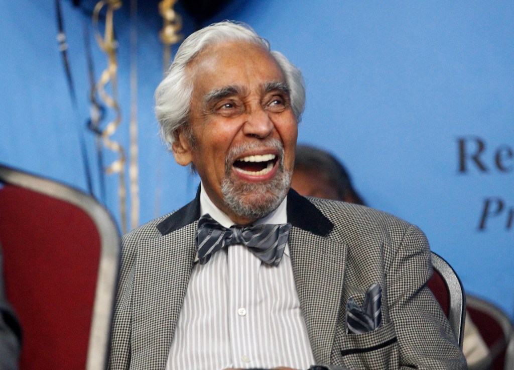 Rev. Al Sharpton laughing in a suit at his 68th birthday event, with high-profile officials including Charles B. Rangel in attendance at the National Action Network in Harlem, N.Y.