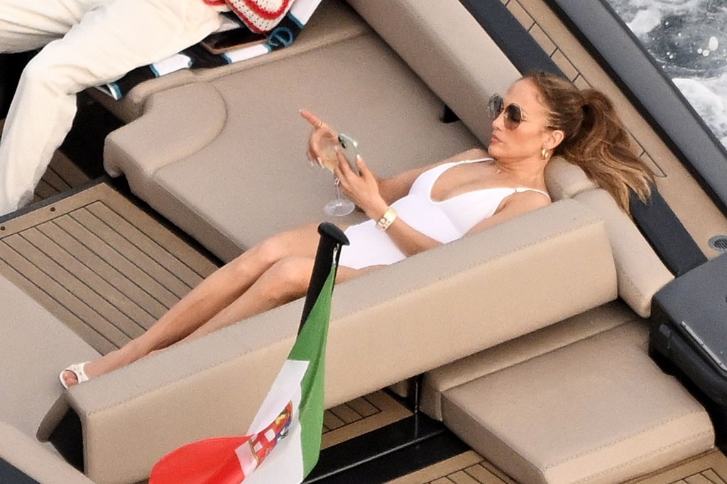 Jennifer Lopez sipping wine and looking at her phone on a boat in Italy. 