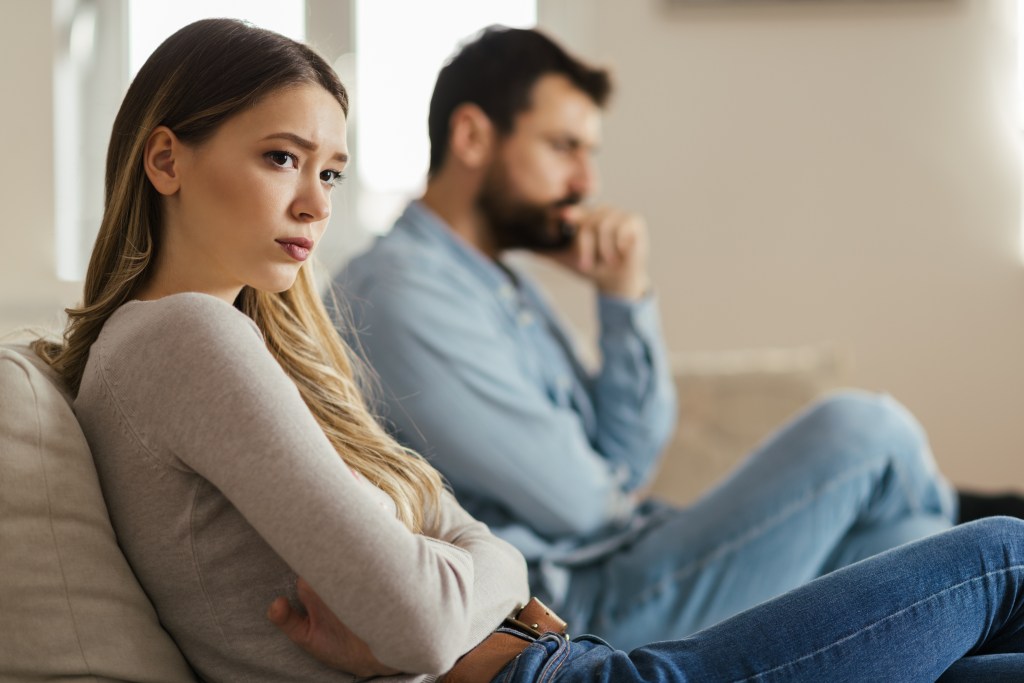 Young anxious woman ignoring her boyfriend while sitting on a couch at home