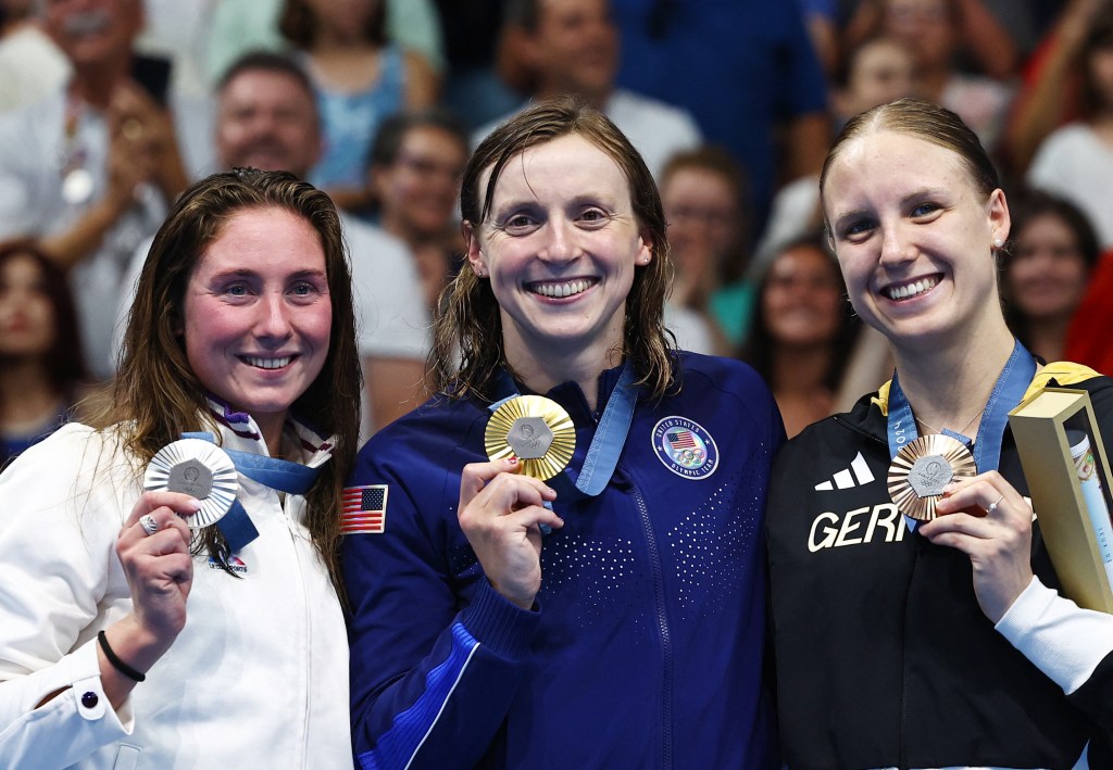 Katie Ledecky (c.) holds up her gold medal along with silver medalist Anastasiia Kirpchnikova (l.) and bronze medalist Isabel Gose (r.) after winning the 1500m freestyle on July 31, 2024.