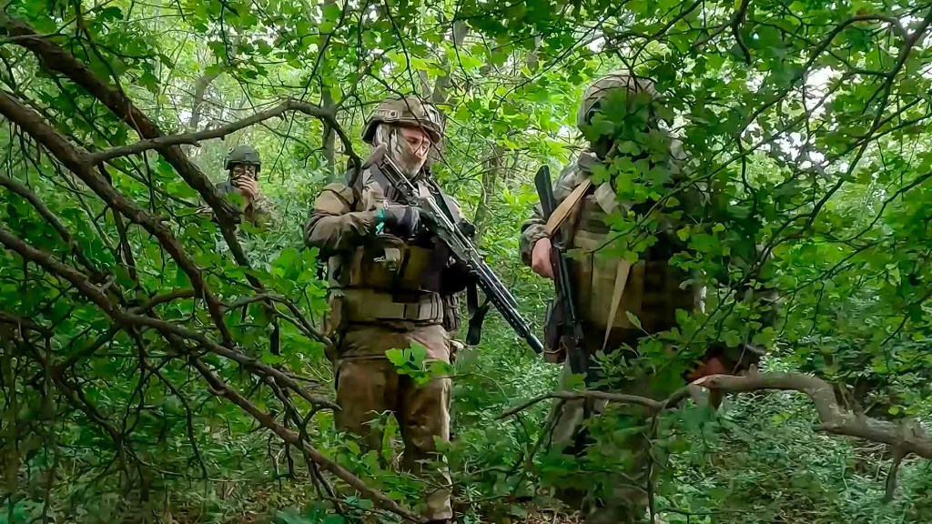 Russian soldiers wearing khaki green combat gear and carrying long guns walk through a forest in an undisclosed location in Ukraine. 