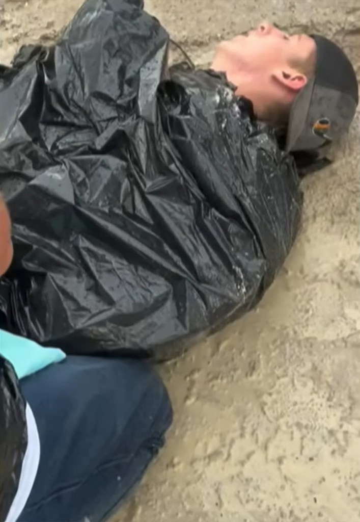The camera pans down to Johnson, seemingly unconscious and lying motionless on the ground with a black garbage bag wrapped around his body.
